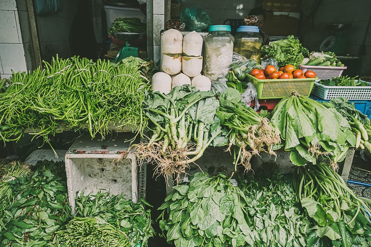 Verse groenten uitgestald bij een marktkraam, die doet denken aan streetfood van Azie, zoals bladgroenten, lange groene bonen, witte radijsjes, tomaten en kruiden - gerangschikt in kleurrijke bossen en manden voor een overvloedig assortiment.