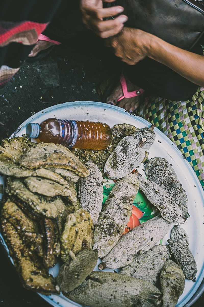 Een groot wit dienblad bevat verschillende stukken honingraat en een plastic fles gevuld met honing. Vlakbij rusten de handen en benen van een persoon op een donker oppervlak - een authentieke Streetfood van Azie marktscène.