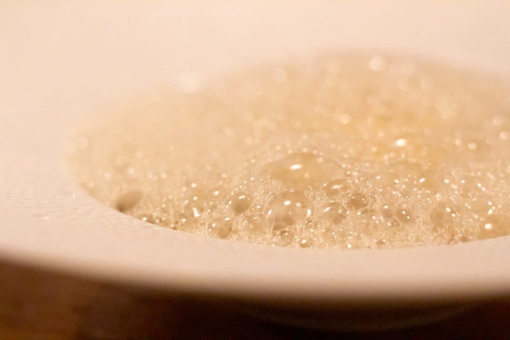 Een close-up van een witte kom gevuld met lichtbruin schuim en bubbels, waardoor een schuimige textuur ontstaat. Het beeld is zacht gefocust en roept het romige uiterlijk op van de specialiteiten van Uitboeren in Den Bosch.