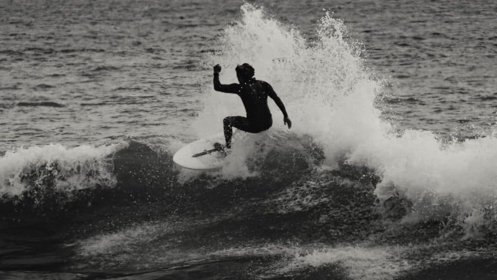 Een surfer in een wetsuit berijdt een golf, midden in de actie vastgelegd terwijl het water om hem heen spuit. Het zwart-witbeeld benadrukt de dynamische beweging en het contrast, waardoor de sensatie van surfen perfect wordt vastgelegd - een van de beste wat doe-ervaringen in Costa Rica.
