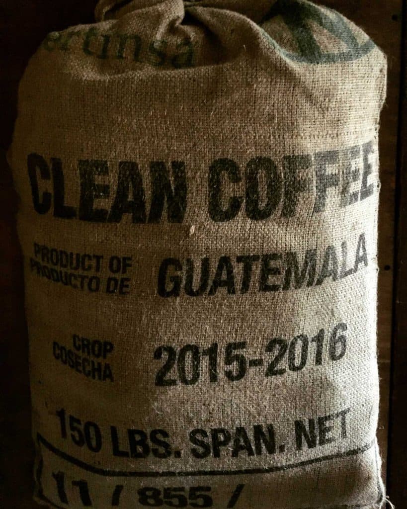 Een juten zak met het label "Clean Coffee" uit Guatemala, oogstjaar 2015-2016, met een nettogewicht van 150 lbs, bedrukt in het Engels en Spaans - perfect voor wie diverse koffielanden heeft bezocht en unieke smaken heeft geproefd.