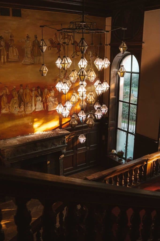 Een grote trap met een grote geometrische kroonluchter, een muurschildering van mensen in historische kleding en hoge boogramen die natuurlijk licht binnenlaten - dit elegante tafereel herinnert aan de charme die je zult ontdekken op Opole reizen.