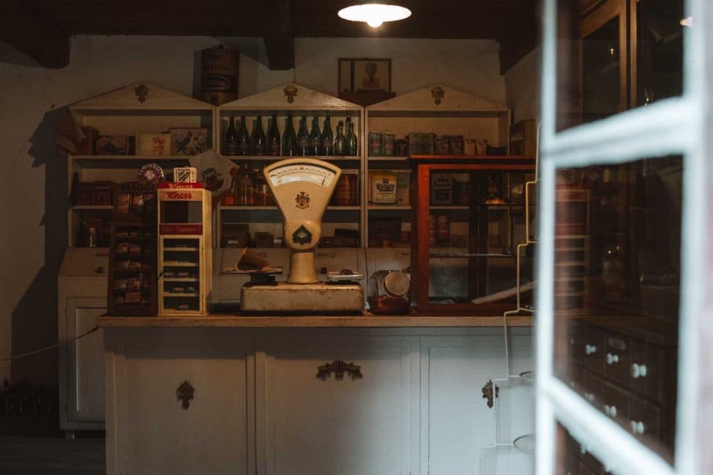 Een vintage winkelinterieur in Opole reizen, met houten planken vol oude blikken, dozen en flessen achter een witte toonbank. Een grote, ouderwetse weegschaal staat op de toonbank onder warme verlichting.