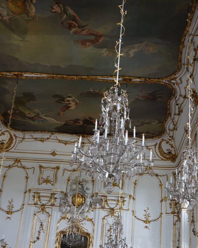 Een weelderige barokke kamer voor een prinses, met versierde gouden en witte muren, een grote kroonluchter met kristallen hangers en spiegels die elk elegant detail weerspiegelen - een sprookjesachtige omgeving in Tsjechië voor slechts een prikje.