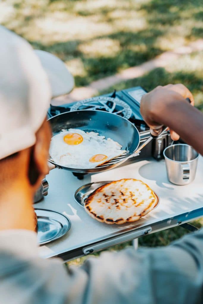 Iemand die eieren bakt in een koekenpan op een draagbaar fornuis naast een gebakken flatbread op een tafel in de open lucht, waarmee de sfeer van de Albanese nomaden wordt vastgelegd tijdens een avontuurlijke roadtrip door Albanië.