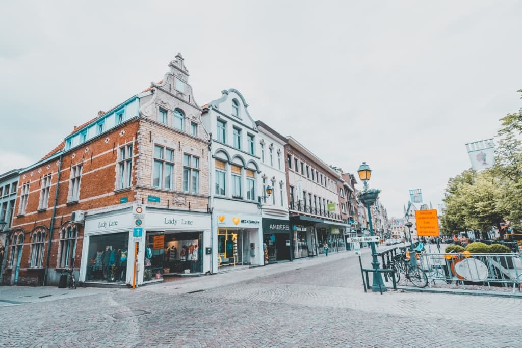 Een brede straat met kinderkopjes omzoomd met historische Europese gebouwen en winkels zoals "Lady Line" roept de charme van het stadsleven op - perfect voor wie droomt van slapen op een laars in Mechelen na het verkennen van bruisende trottoirs en lommerrijke bomen.