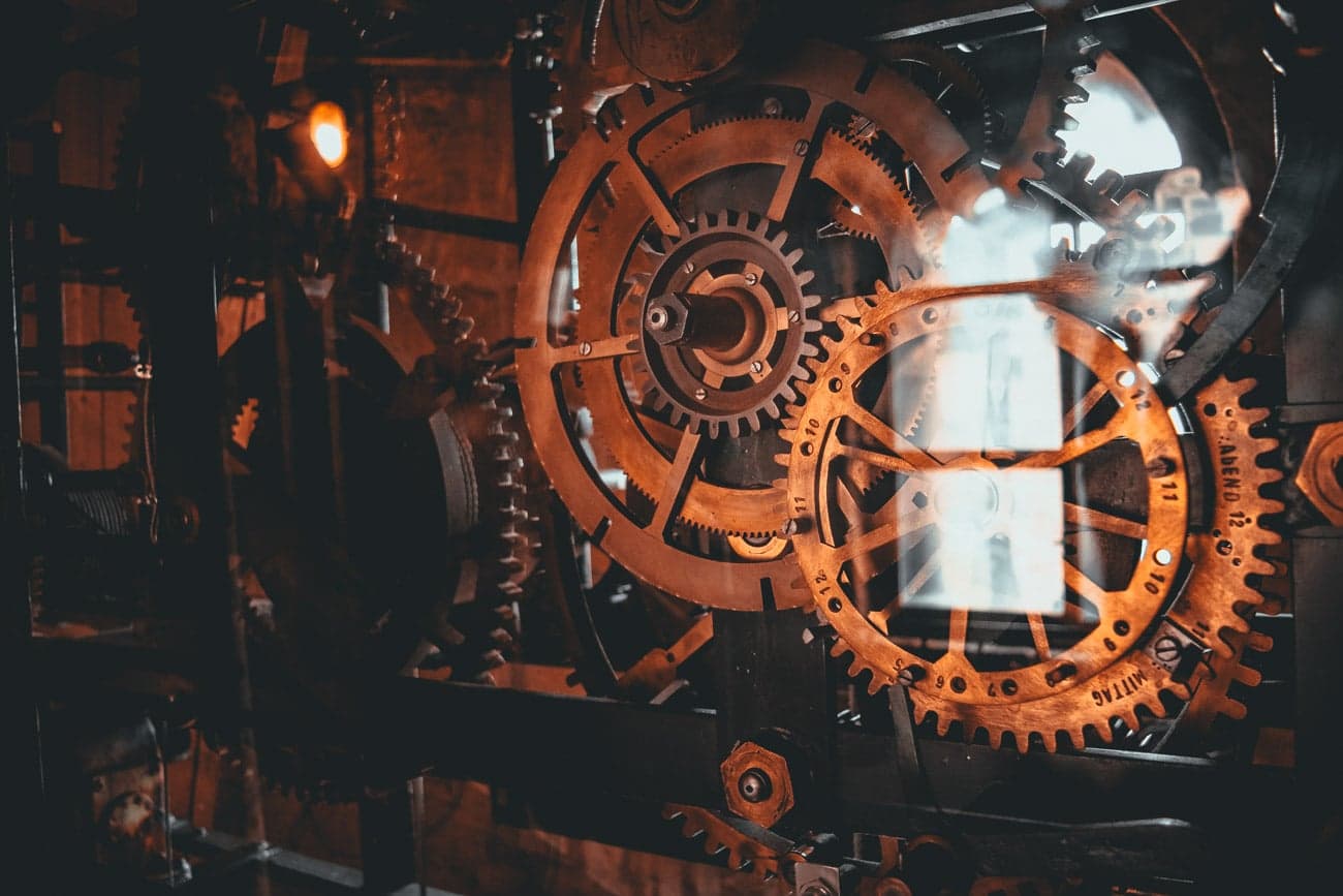 Close-up van grote, in elkaar grijpende bronzen tandwielen en radertjes in een mechanisch uurwerksysteem, warm verlicht - een echo van de vintage, steampunk-esthetiek die je tegenkomt als je de ingewikkelde technische hoogstandjes ontdekt.