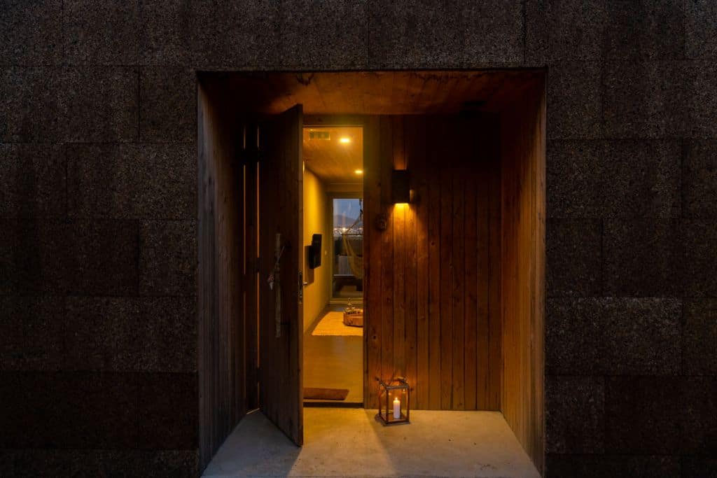 Een warm verlichte houten voordeur staat gedeeltelijk open en onthult een gezellig interieur met een hal en een glimp van een woonruimte. Dit biedt de uitnodigende sfeer die je vaak aantreft in de beste hotels die Sao Miguel te bieden heeft. Een verlichte lantaarn staat bij de ingang en verwelkomt gasten binnen.