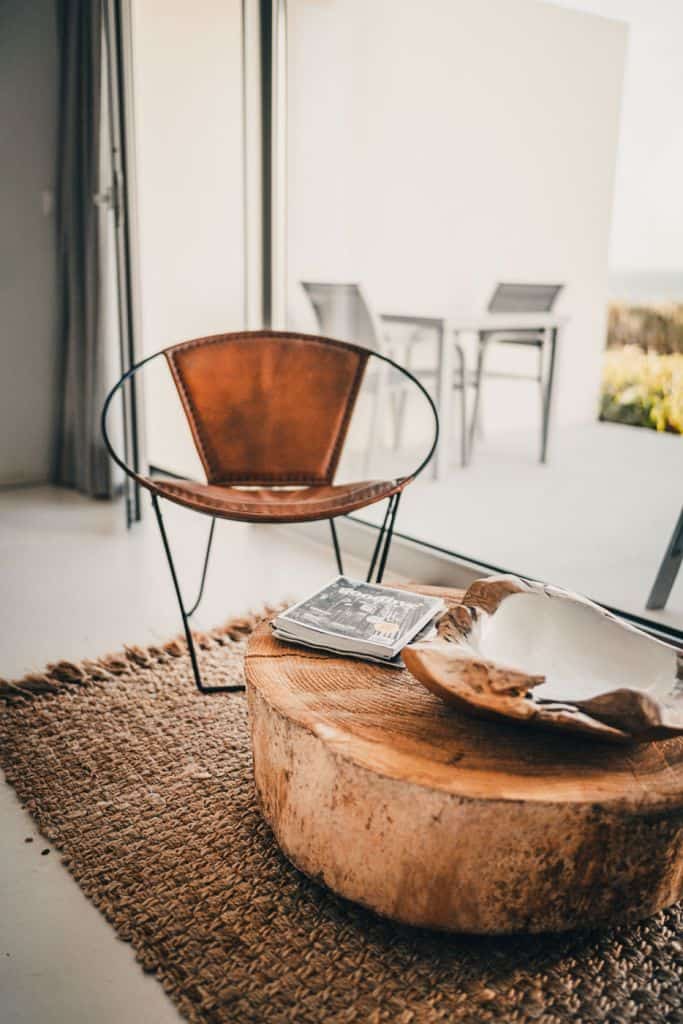 Een moderne, minimalistische leefruimte met een leren stoel met een metalen frame, een stevige houten salontafel met tijdschriften, zoals gidsen voor de beste hotels die Sao Miguel te bieden heeft, een geweven vloerkleed en glazen deuren die openen naar een lichte patio met buitenstoelen.