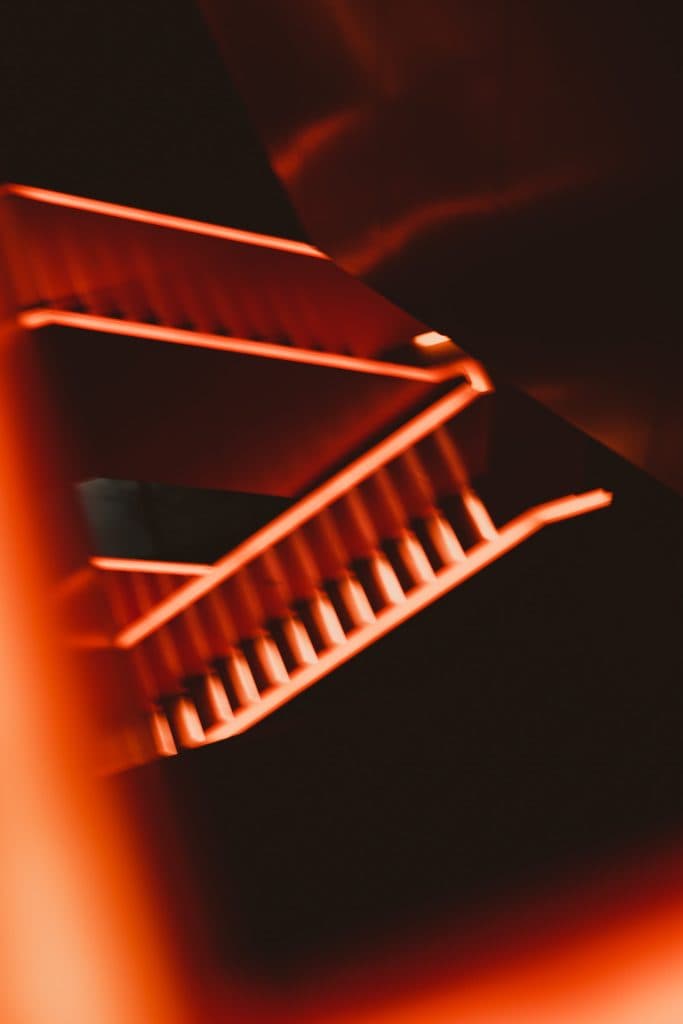 Abstracte afbeelding van een wenteltrap van bovenaf gezien, met gloeiende oranjerode lichten die de trap tekenen tegen een donkere achtergrond. Deze artistiek vervaagde foto legt dramatische verlichting en geometrische vormen vast, perfect voor fotolocaties Ruhrgebied.