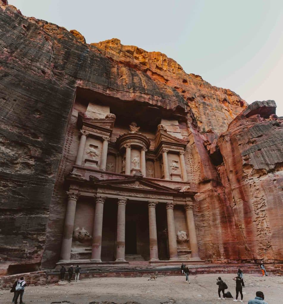 Een uitzicht op Petra's beroemde Al-Khazneh (De Schatkamer), een van de hoogtepunten van Jordanië, laat toeristen zien die staan en foto's nemen voor de oude tempel die is uitgehouwen in opvallende rode zandstenen kliffen.
