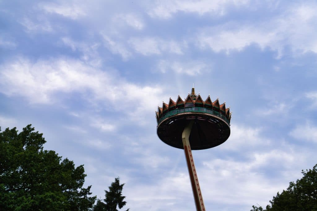 Een hoge pretparkattractie met een ronde, pagodeachtige structuur aan de bovenkant rijst op boven groene bomen onder een blauwe wolkenhemel - perfect voor wie een vakantie met kinderen plant of kaartjes voor de Efteling wil kopen.