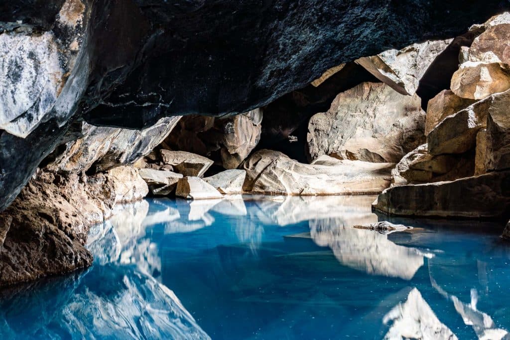 Een rustig, blauw geothermisch zwembad in een rotsachtige grot waar het zonlicht naar binnen schijnt. Een onvergetelijk gezicht tijdens je 7-daagse roadtrip met Iceland Nomads, waar de wanden van de grot gloeien en het heldere water het avontuur van Roadtrip IJsland weerspiegelt.