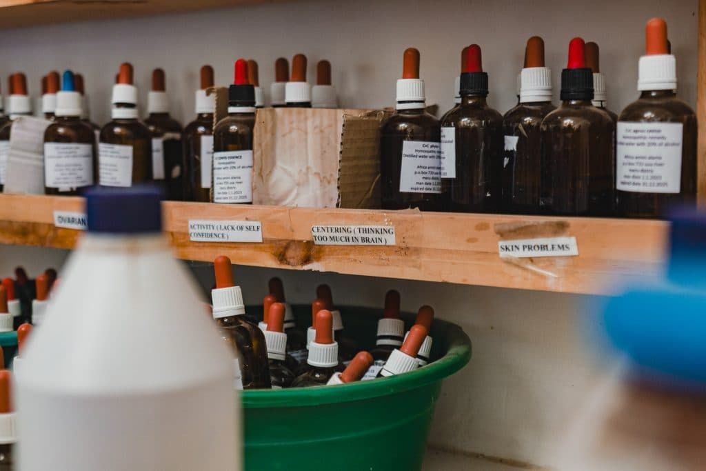 Glazen flesjes met druppeldoppen, gelabeld voor gebruik als "huidproblemen" en "gebrek aan zelfvertrouwen", staan op planken en in een groene container, die doet denken aan hoe Tanzania hoogtepunten essentiële momenten vastlegt in doordacht detail.