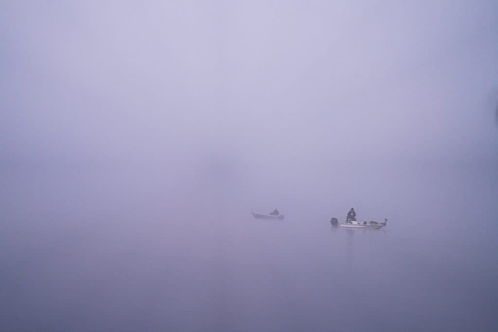 Twee kleine boten dobberen op kalm water omgeven door dichte mist in Zweden, met zwakke reflecties en weinig zichtbare details, waardoor een serene en mysterieuze sfeer ontstaat.