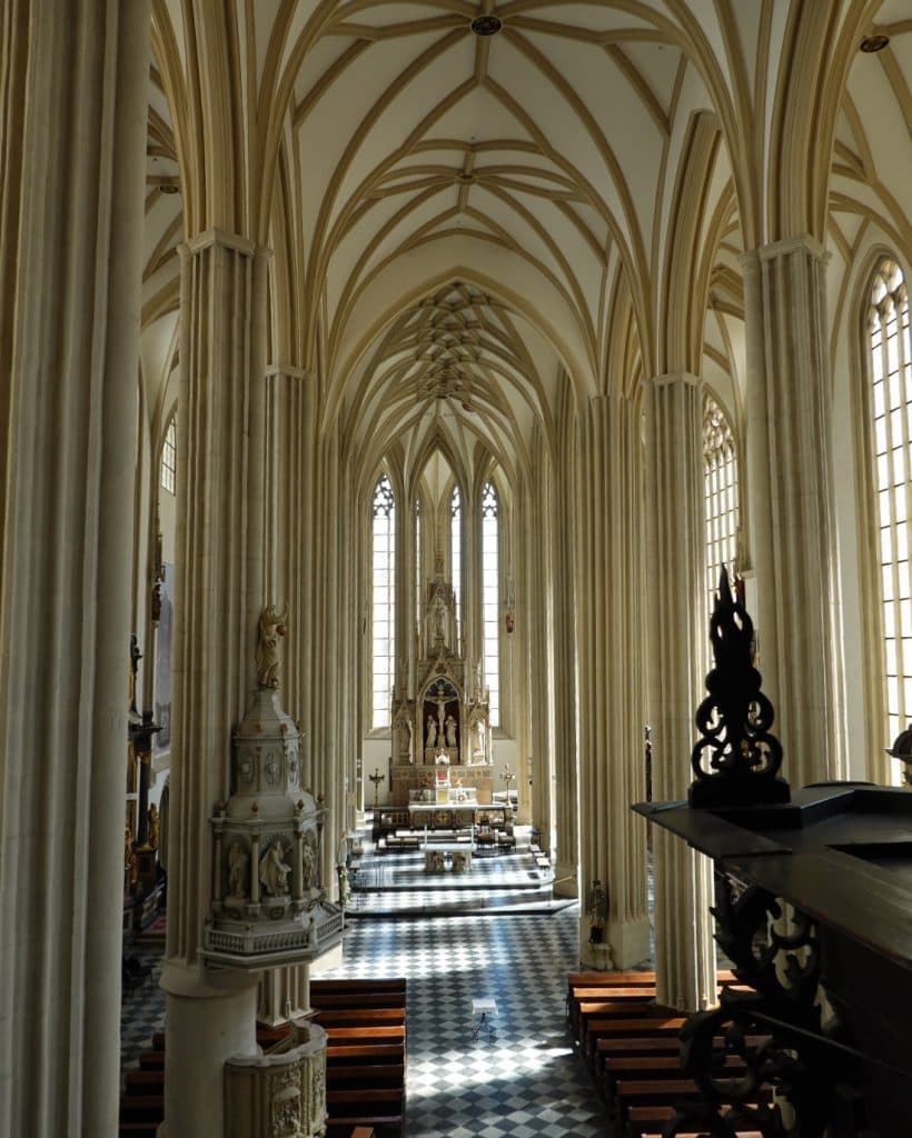 Interieur van een grootse gotische kathedraal in Brno, Tsjechië, met hoge spitsbogen, een geribbeld gewelf en slanke zuilen. Zonlicht stroomt door de glas-in-loodramen en verlicht de houten kerkbanken en het sierlijke altaar. Perfect voor reisinspiratie.