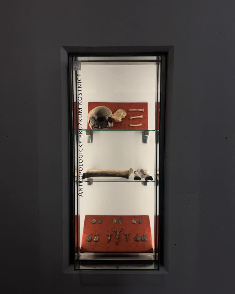 Een glazen vitrine in het Tsjechische Brno heeft planken met een menselijke schedel, lange botten, metalen pijlpunten of gereedschappen en kruizen en medaillons op rode stof - een intrigerende antropologie-expositie voor wie van reizen en geschiedenis houdt.