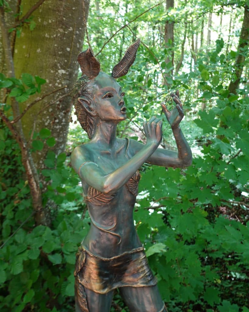 In een weelderig bos bij Morges, in het kanton Vaud, staat een bronzen beeld van een bosnimf of faun met puntige oren en hoorns bedekt met bladeren. De figuur draagt een topje en een rok met bladmotief en heeft haar armen gracieus opgeheven te midden van het dichte gebladerte en het gevlekte zonlicht aan de oever van het meer.