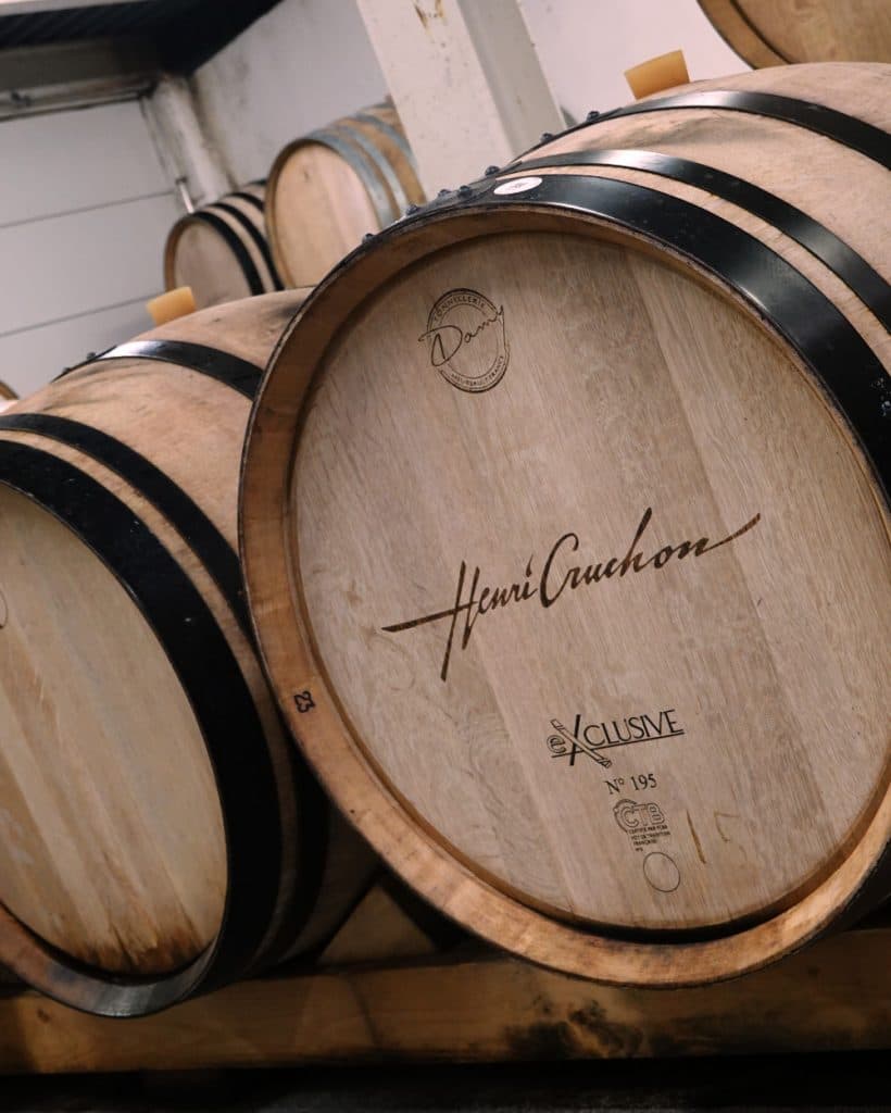 Close-up van grote houten wijnvaten die in een kelder bij Morges, in het kanton Vaud, op elkaar zijn gestapeld. Op het vat vooraan staat „Henri Giraud Xclusive No. 195” vermeld; het is voorzien van zwarte metalen banden en heeft een lichtbruine houtstructuur. Op de achtergrond staan nog meer vaten opgesteld onder een wit plafond.