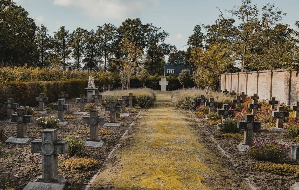 Een begraafplaats met stenen kruisen die de graven markeren, een centraal pad, bomen eromheen en een standbeeld dat aan het einde van het pad te zien is – een onverwacht vredige omgeving die in schril contrast staat met de ‘Bruisend Breda’-sfeer en momenten van bezinning op ‘het goede leven’ oproept.