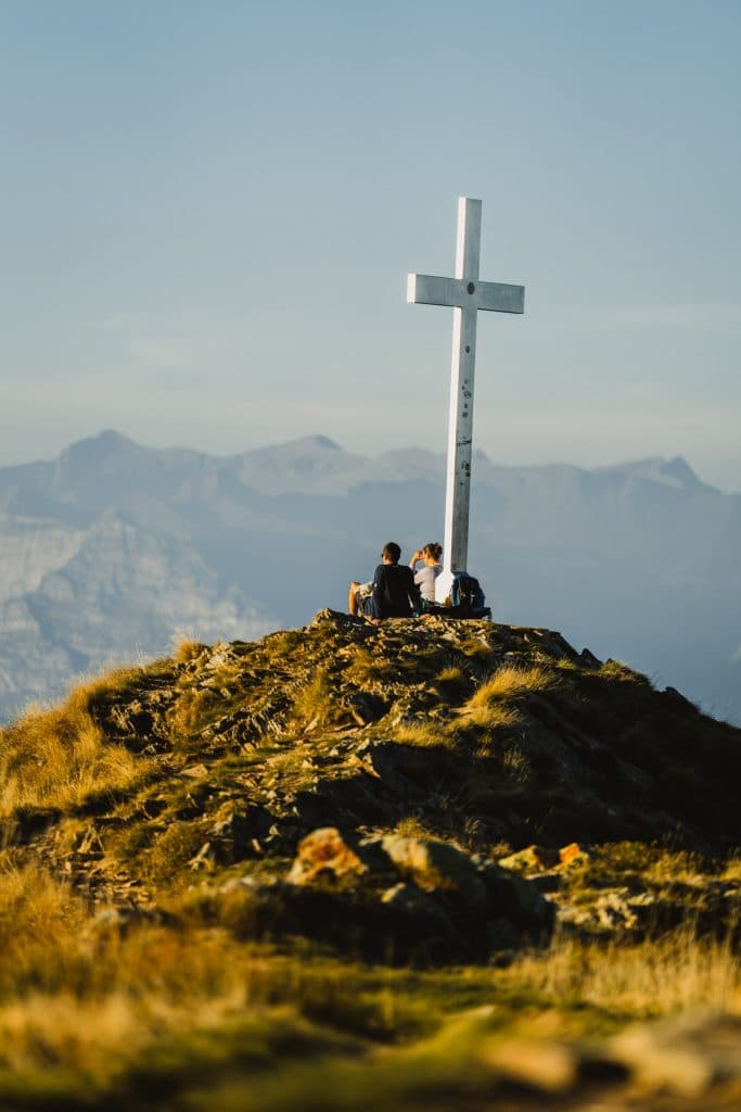 Het witte kruis op de top van de Monte Gambarogno, op 1.734 meter, met wandelaars die ernaast zitten en de Alpen erachter.