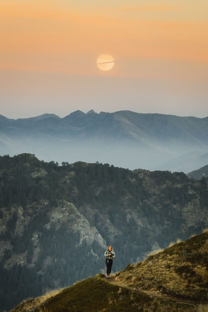 De volle oogstmaan komt op boven de bergen van Ticino, terwijl een wandelaar op de helling van de Monte Gambarogno staat.