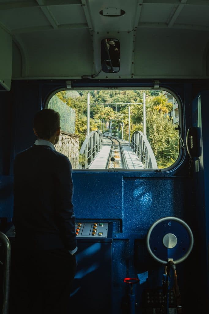 Een man staat vooraan in de blauwe cabine van het kabelspoor van Locarno naar Orselina en kijkt door het raam naar de rails.