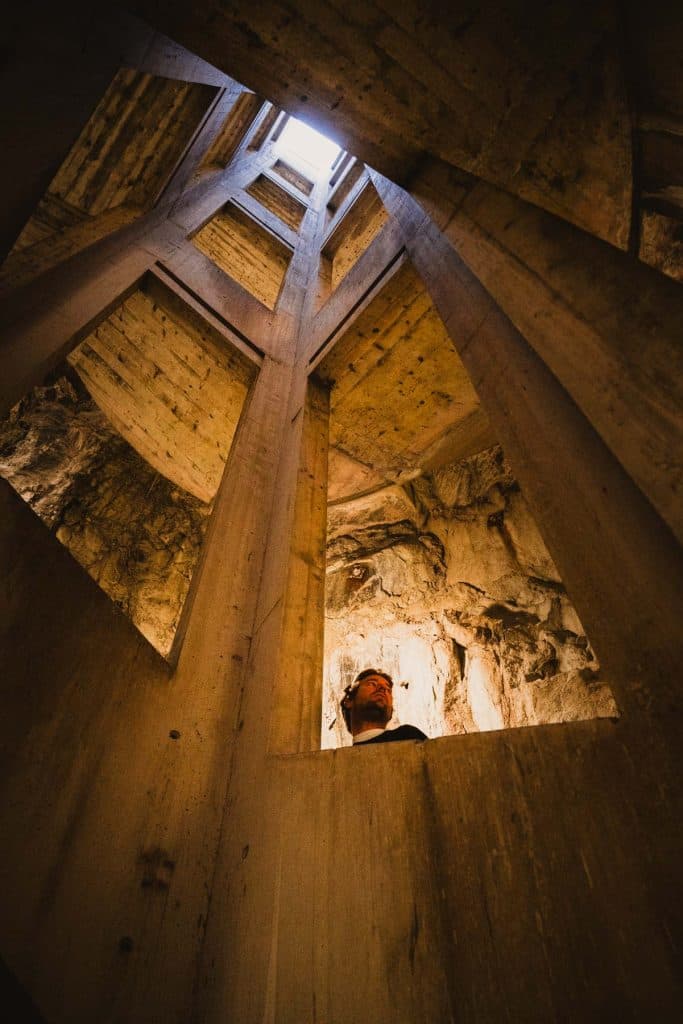 Zicht naar boven in de betonnen liftschacht van Castelgrande in Bellinzona, waar licht door de rots naar binnen valt.
