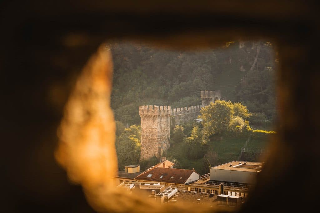 Door een opening in de muur van Castelgrande zie je Castello di Montebello op de heuvel boven de daken van Bellinzona.