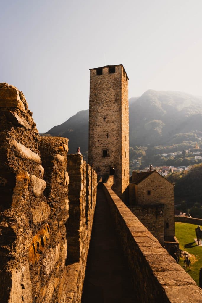 De stenen verdedigingsmuur van Castelgrande in Bellinzona, met een vierkante middeleeuwse toren tegen de bergen.