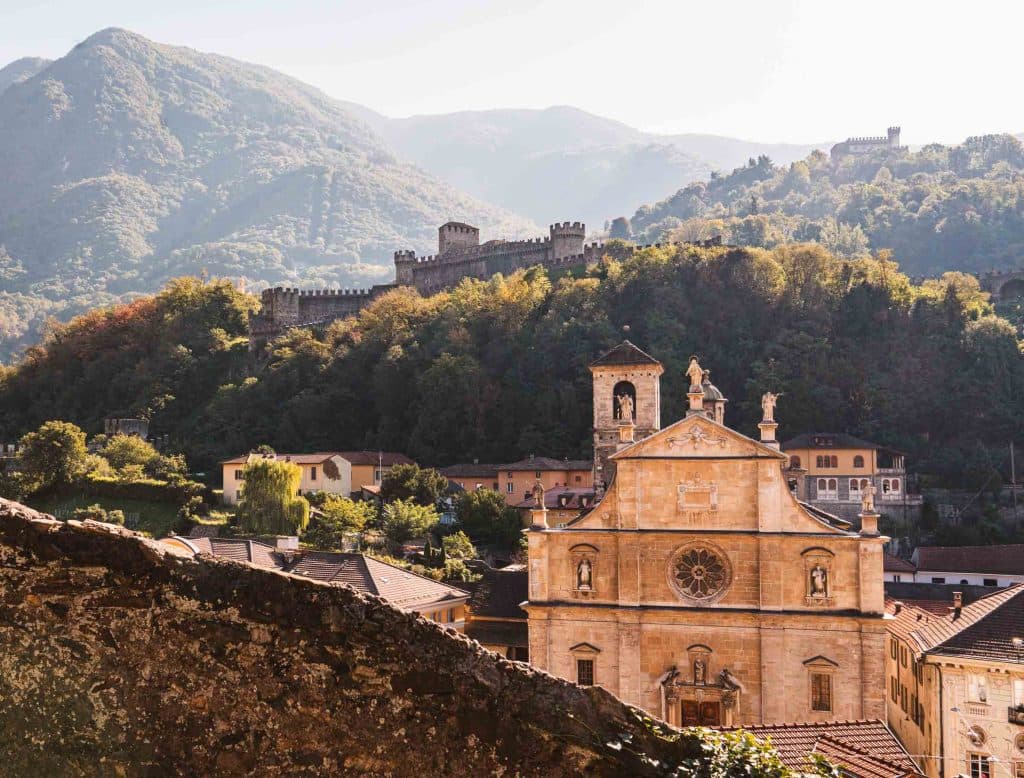 De barokke gevel van de Collegiata in Bellinzona, met Castello di Montebello op de beboste heuvel erachter.