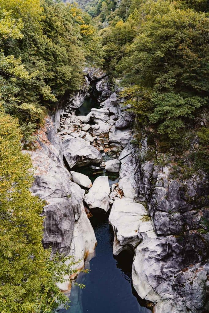 De Verzasca slingert door een diepe kloof van gladde grijze rotsen, tussen het groen van de vallei.