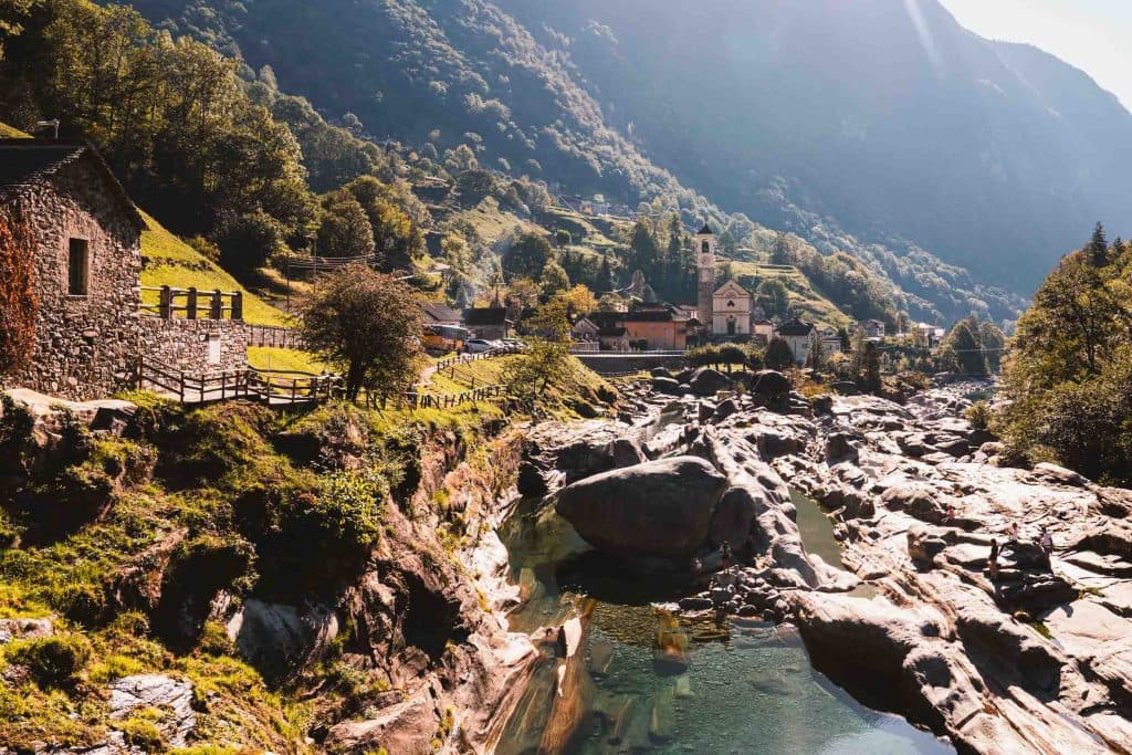 Stenen huizen en een kerktoren aan de oever van de Verzasca bij Lavertezzo, tussen grote rotsblokken en helder water.