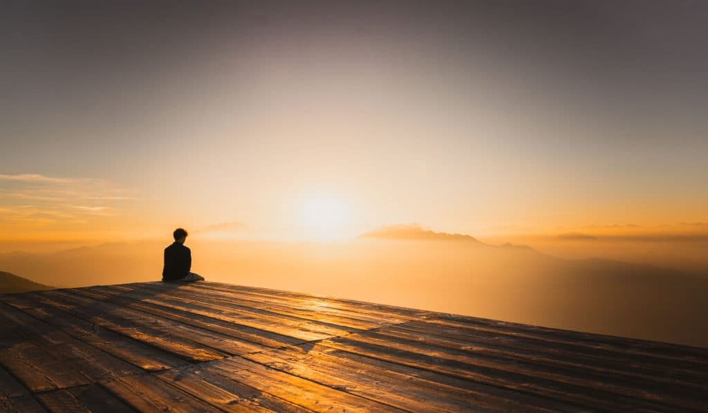 Iemand zit op een houten terras op de Monte Gambarogno en kijkt naar de zon die ondergaat boven de nevel en het Lago Maggiore.