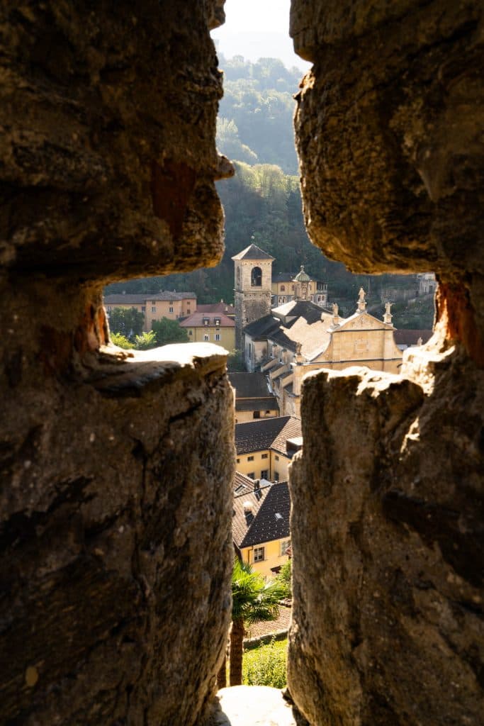 Door een schietgat in de muur van Castelgrande zie je de kerktorens en daken van Bellinzona.