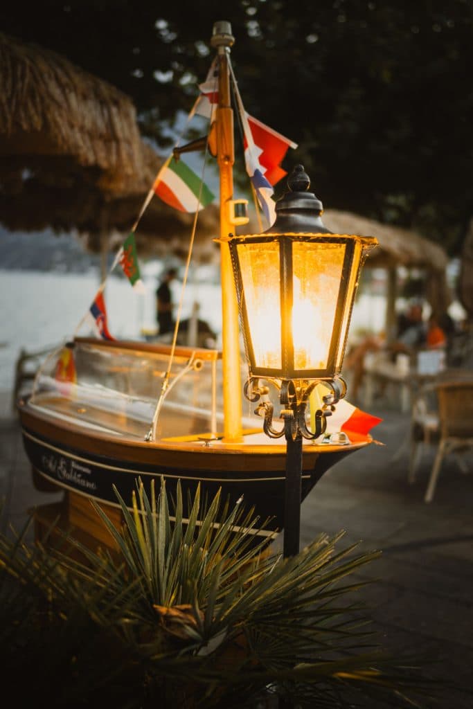 Een brandende lantaarn voor een houten bootje met vlaggetjes aan het haventje van Ascona, 's avonds.