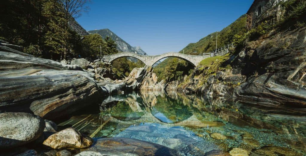 De Ponte dei Salti, de stenen brug met twee bogen in Lavertezzo, weerspiegelt in het heldere water van de Verzasca.